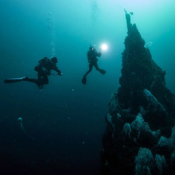 Divers exploring deep wreck pinnacle with torches