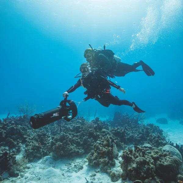 Divers using scooter in open water coral terrain
